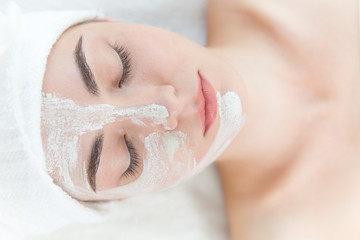 Young beautiful girl face masking relaxing in spa salon eyes closed