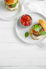 Burgers with grilled beef patties, cream cheese and spinach on classical bun. White wooden background