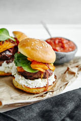 Burgers with grilled beef patties, cream cheese and spinach on classical bun. White wooden background