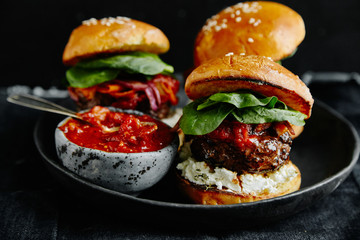 Burgers with grilled beef patties, cream cheese and spinach on classical bun. Dark rustic wooden background