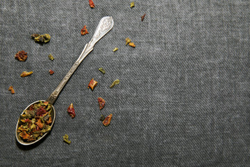 Dried colored pepper in spoon on grey fabric. Spices close up. Space for text on background