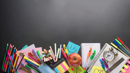 Obraz premium Banner Concept Back To School Alarm Clock Color Chalk Pencil Apple Notebook Stationery on Green Blackboard Background. Design Copy Space Supplies Top View Flat Lay
