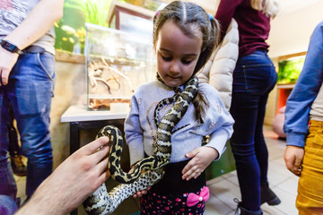 Zoo volunteer showing a snake to a child and letting her touch the snake