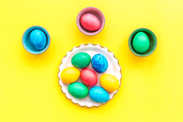 Colorful easter eggs in plate on yellow background top view mockup