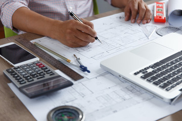 Top view, Architect or engineer hands working on blueprint plans with a pencil ,laptop a ruler, calculator, and engineering tools. Architect or engineer working on blueprint in office.