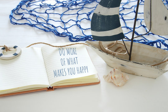 nautical concept image with white decorative sail boat and open notebook: DO MORE OF WHAT MAKES YOU HAPPY.
