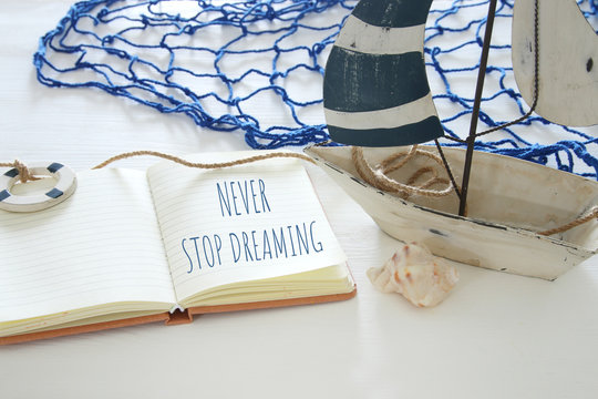nautical concept image with white decorative sail boat and open notebook: NEVER STOP DREAMING.