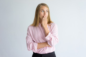 Portrait of young Caucasian woman wearing pink blouse covering mouth afraid to say a word or...