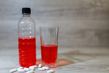 Sports set, energy drink in glass and plastic bottle on wooden table, scattered pills. Energy for workout in a gym.