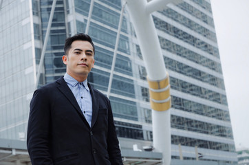 handsome young asian business man wearing modern black suit standing looking into camera in building city background, confident, team leader, successful, manager, portrait and entrepreneurship concept