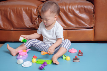 Cute little Asian 18 months / 1 year old toddler boy child sitting on floor near sofa in living room at home having fun playing alone with cooking toys , Educational toys for young children concept