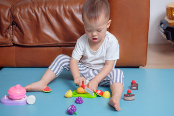 Cute little Asian 18 months / 1 year old toddler boy child sitting on floor near sofa in living room at home having fun playing alone with cooking toys , Educational toys for young children concept