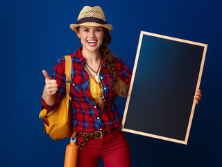 smiling woman hiker showing thumbs up and showing blank board