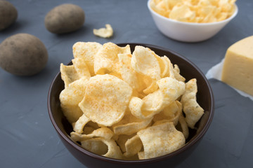 Potato chips with cheese in a plate that is located on a gray background.