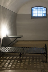 The old prison cell in which the bed, table, lamp, window with a lattice