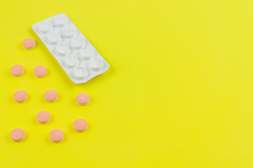Scattered pills beside used white blister pack on background of yellow paper