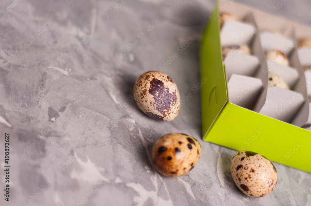 Wall mural One green rectangle cardboard box with lot of spotted fresh quail eggs and scattered three eggs on old broken worn gray cement floor with copy space