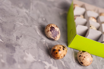 One green rectangle cardboard box with lot of spotted fresh quail eggs and scattered three eggs on old broken worn gray cement floor with copy space
