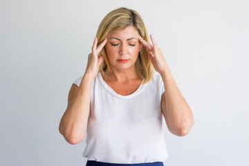 Stressful mature woman suffering from headache and touching temples. Serious concentrated lady...