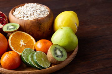 Bowl with oatmeal flakes served with fruits on wooden tray over rustic background, flat lay, selective focus