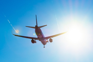 Fototapeta na wymiar Passenger aircraft flies near the sun glare on landing, with the wings of a steam jet vortex.