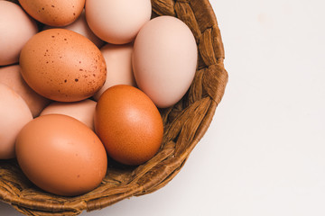 Colored chicken eggs in a wicker brown basket on a light background