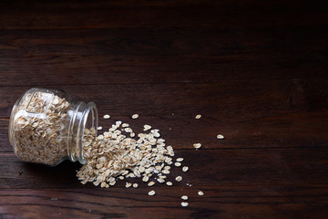 Overturned glass jar and spoon with raw oatmeal on vintage wooden background, close-up, selective focus.
