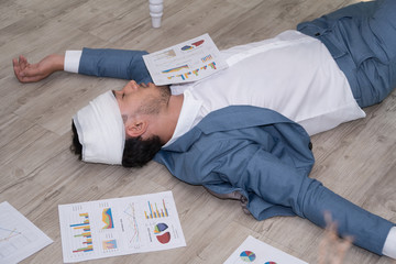 Sick businessman sleeping on floor while using laptop to work hard at office