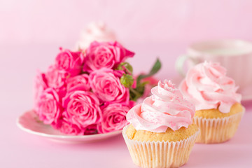 Cupcake with pink cream decoration and roses on pink pastel background.