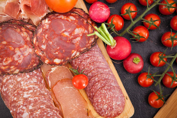 Meat appetizers next to cherry tomatoes, radish and green onion on wooden board