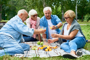 Full length portrait of happy senior people enjoying picnic on green lawn in park chatting and laughing happily on sunny summer day