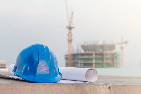 The blue safety helmet and the blueprint at construction site with crane background