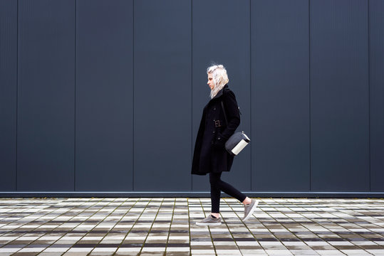 Young Woman Walking In Front Of Minimalist Modern Wall