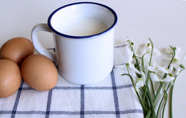 Breakfast scene with mug of milk, tea towel and bouquet of snowdrops. Spring composition. Easter concept.