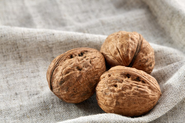 A stack of hard shells of walnuts piled together on light grey fabric cotton tablecloth, selective focus
