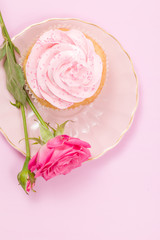 Cupcake with pink cream decoration and roses on pink pastel background.