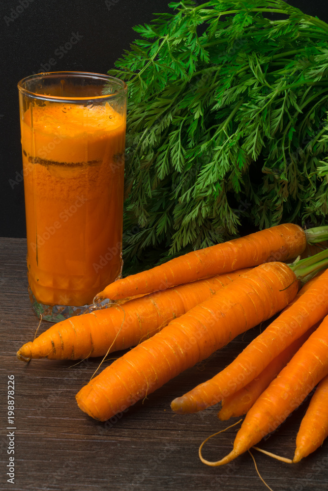 Wall mural fresh carrot juice and bunch of carrot on the black table