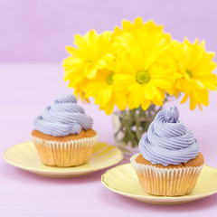 Cupcakes decorated with violet cream and bouquet of yellow chrysanthemums on violet pastel background with text area for greeting banner.