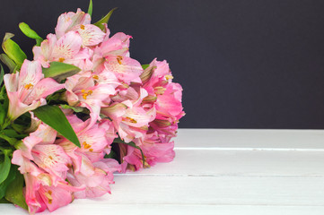 Beautiful pink alstroemerias on a white woodent planks against a black background (copy space)
