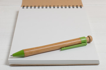 Pen of natural wood and a notebook on a white table.