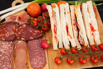 Delicious club sandwiches next to appetizers and cherry tomatoes