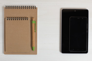 Pen of a natural wood smartphone and notebook on a white table.