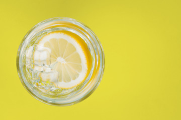 Drink, water with lemon in a glass, on a yellow background.