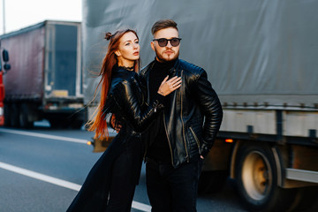 red skinny girl in a black dress stands together with the bearded guy on the highway