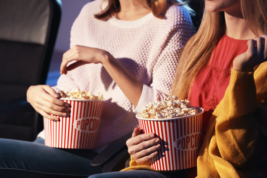 Young women with tasty popcorn in cinema