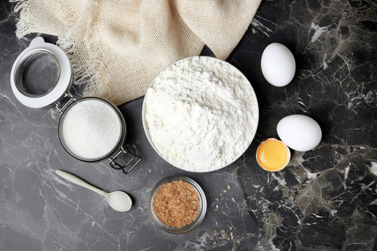 Bowl with flour, eggs and sugar on grey background, top view