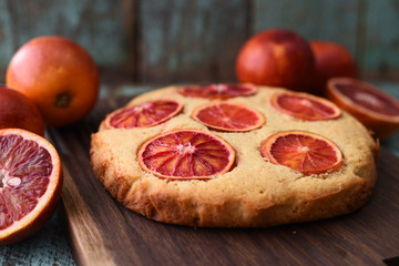 Homemade imperfect cake with blood orange slices on dark oak board