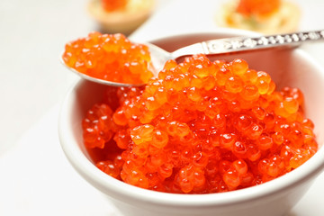 Spoon and bowl with delicious red caviar on light background, closeup