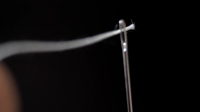 Threading the eye of a needle. Pulling the thread into the needle eye of the sewing needle.