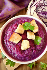 Cream soup made of red cabbage with croutons and parsley on wooden table